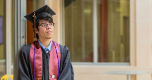 Dell Scholar stands in graduation cap outside his university